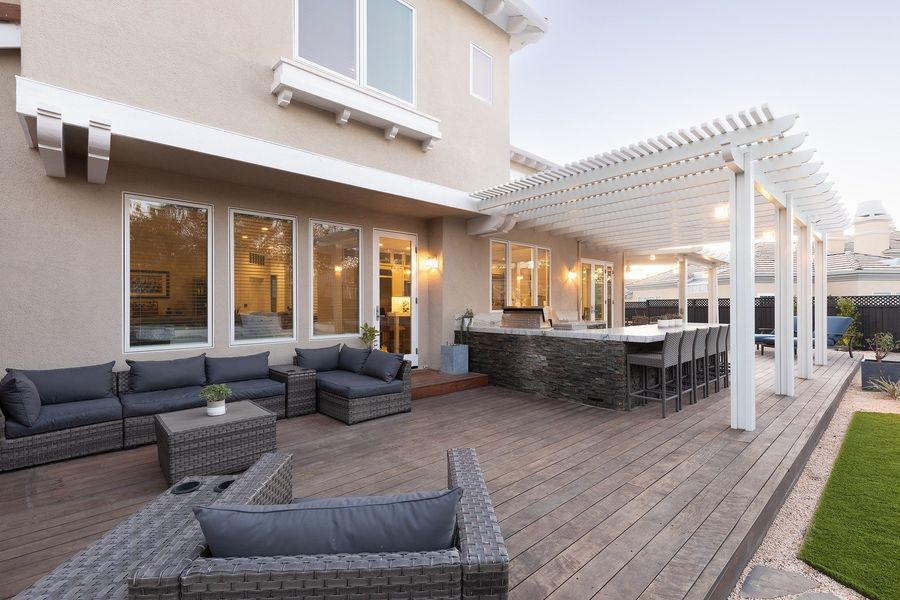 Deck sectional and lounge chairs beside the house, with the pergola and stone-clad bar counter beyond