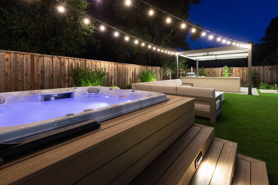 Swim spa lit on the composite deck, lounge seating and pergola beyond