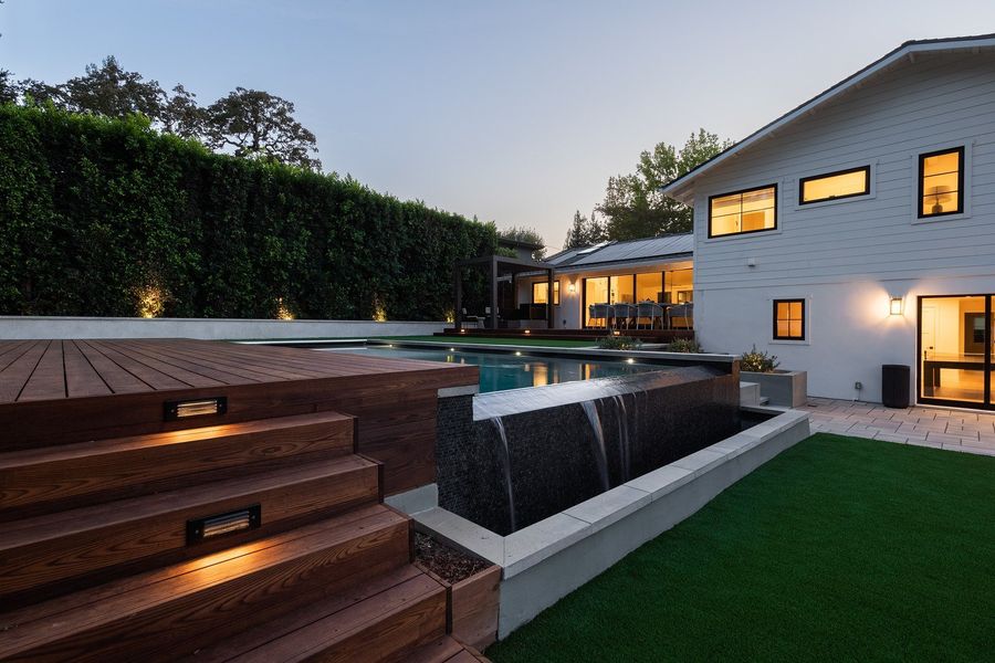 Hardwood steps with recessed lights beside a dark stone water feature wall and lawn at twilight