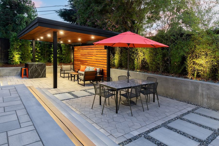 Patterned paver dining terrace with a stone-topped table, pebble-jointed concrete pads and a concrete retaining wall