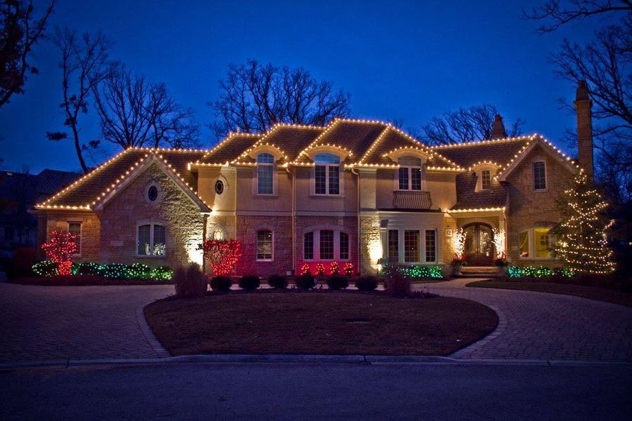 Two-story home outlined in warm white and color lights at dusk